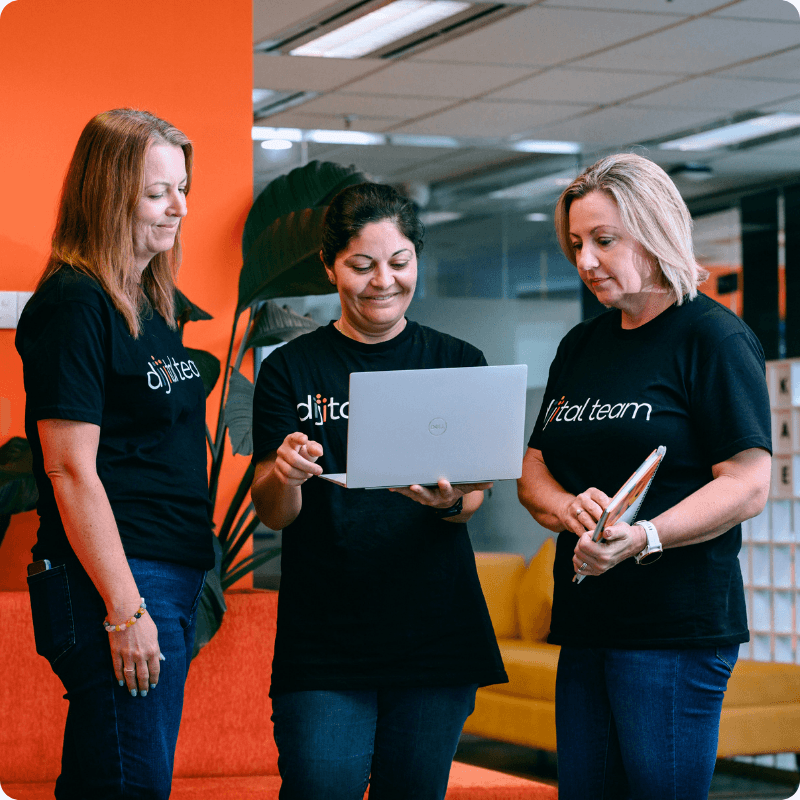 Three Dijital Team members in branded t-shirts reviewing work on a laptop